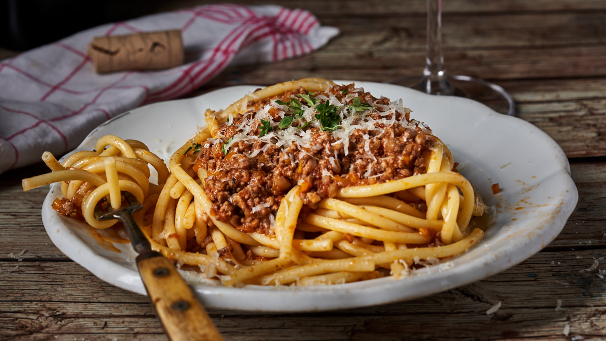 image of Spaghetti Bolognese, an italian classic dish of slow cooked meat in a tomato sauce, served with spaghetti on a white plate in a rustic setting