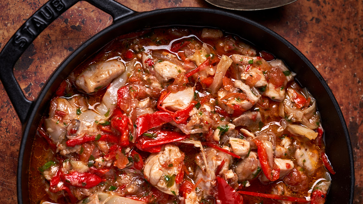 Image of tuscan stewed chicken and peppers in a black cast iron pan against an ochre background