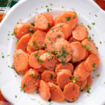 image of carote in agrodolce (sweet and sour carrots) served on a white plate against a wooden background
