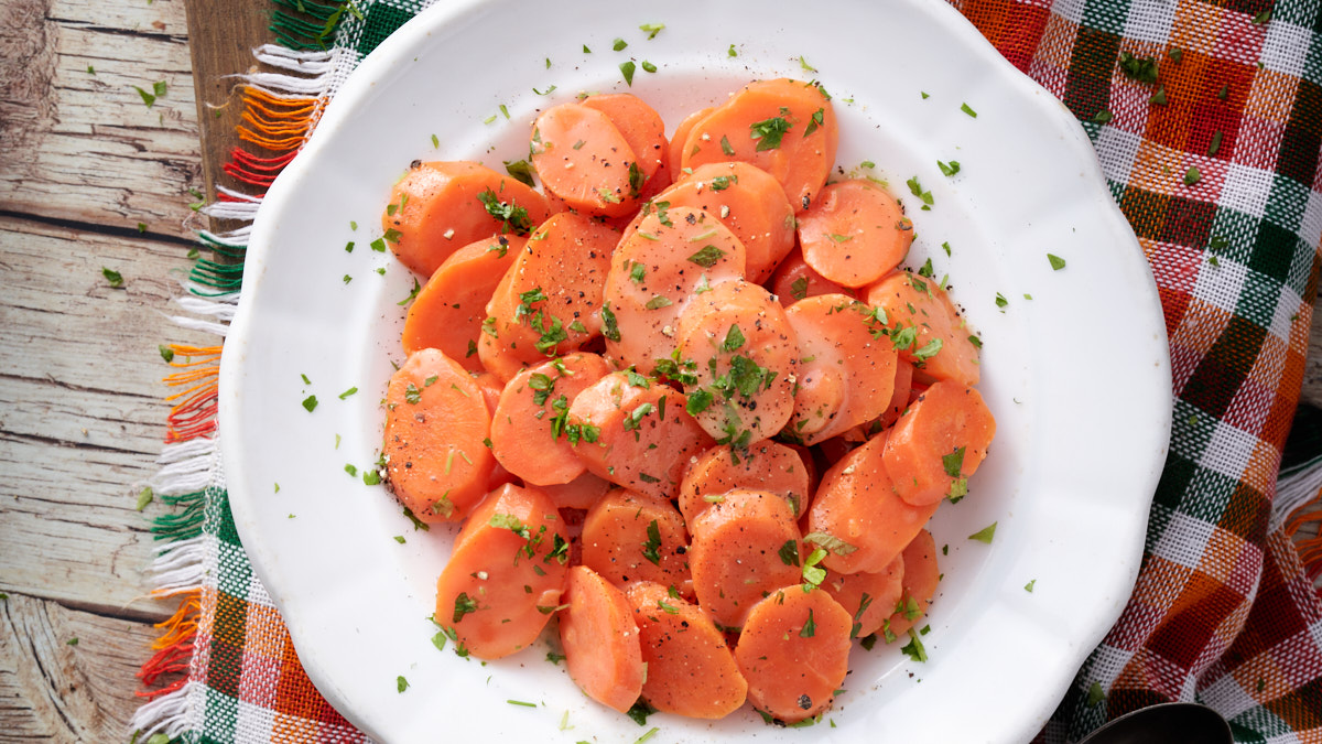image of carote in agrodolce (sweet and sour carrots) served on a white plate against a wooden background