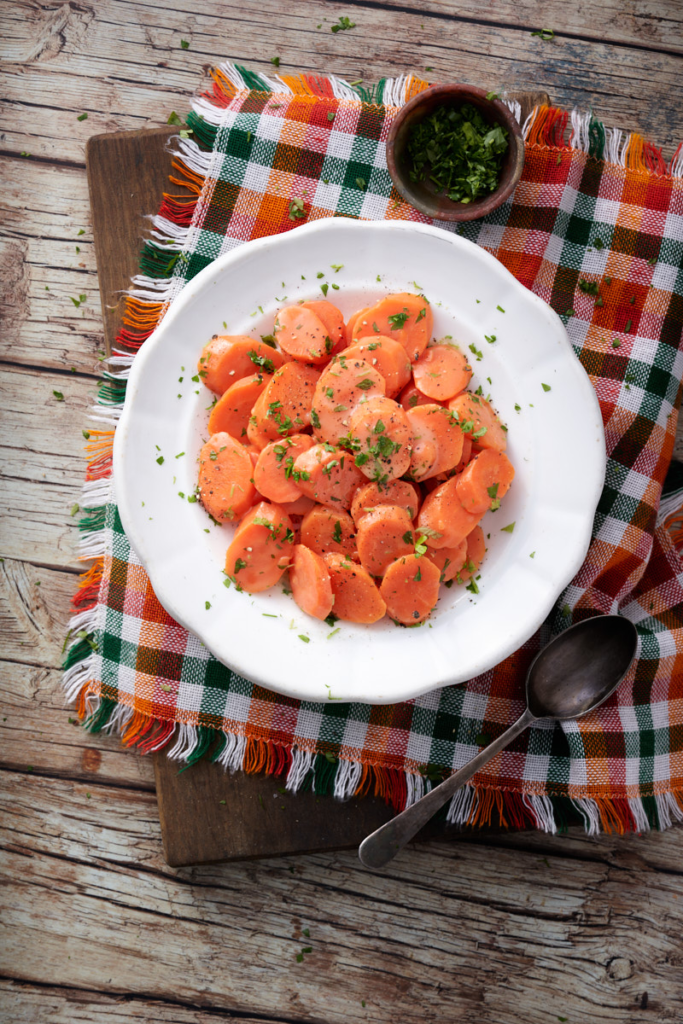 image of carote in agrodolce (sweet and sour carrots) served on a white plate against a wooden background