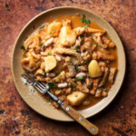 image of trippa in umido with borlotti beans from Friuli served on a rustic plate on an ochre background with a bone handled fork resting on the plate.