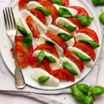 Image of caprese salad of tomatoes, buffalo mozzarella and basil drizzle with olive oil and topped with cracked pepper on a white plate