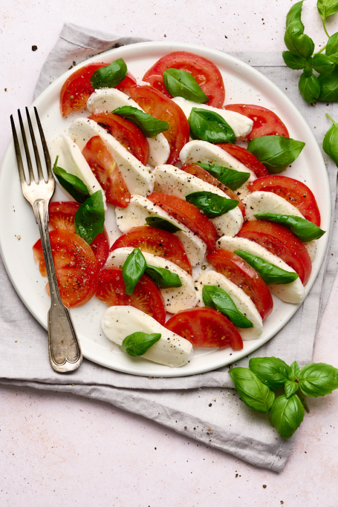 Image of caprese salad of tomatoes, buffalo mozzarella and basil drizzle with olive oil and topped with cracked pepper on a white plate