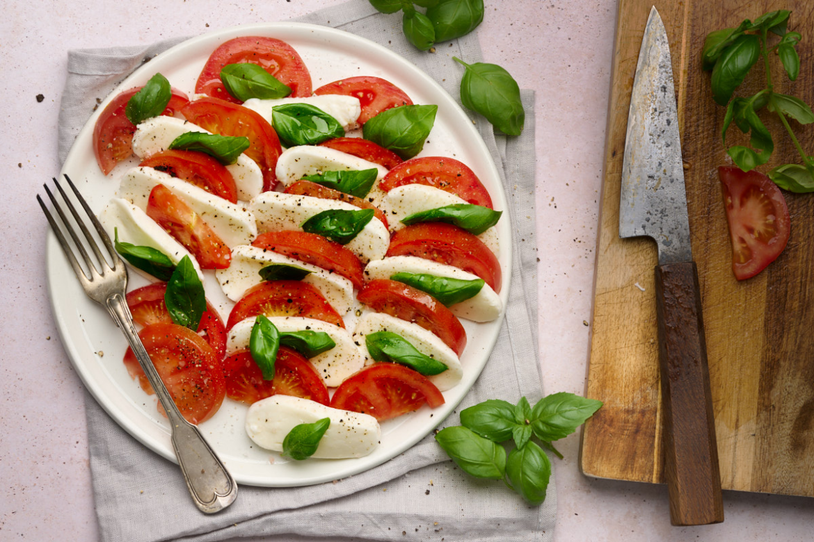 How to Make Caprese Salad Image of caprese salad of tomatoes, buffalo mozzarella and basil drizzle with olive oil and topped with cracked pepper on a white plate