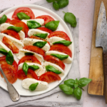 Image of caprese salad of tomatoes, buffalo mozzarella and basil drizzle with olive oil and topped with cracked pepper on a white plate