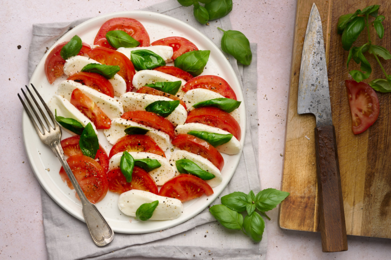 Image of caprese salad of tomatoes, buffalo mozzarella and basil drizzle with olive oil and topped with cracked pepper on a white plate