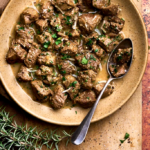 Image of cacio e ova, a traditional Abruzzo Easter lamb stew served in a wide plate on a wooden board, garnished with rosemary