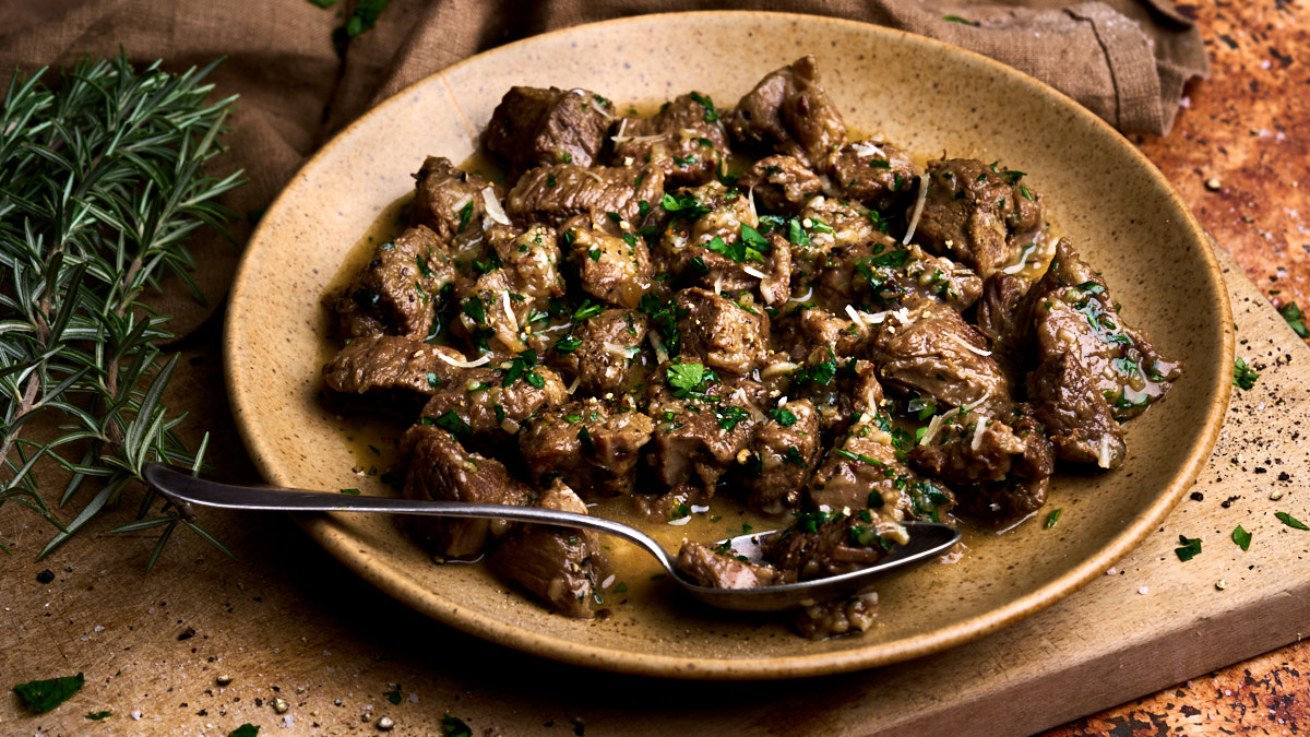 Image of cacio e ova, a traditional Abruzzo Easter lamb stew served in a wide plate on a wooden board, garnished with rosemary
