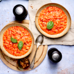 image of Pappa al Pomodoro, a rustic tuscan dish made of tomatoes and stale bread, served into bowls with the red tomato soup contrasting against a light blue background.