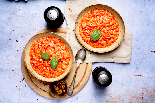 image of Pappa al Pomodoro, a rustic tuscan dish made of tomatoes and stale bread, served into bowls with the red tomato soup contrasting against a light blue background.
