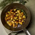 Image of Italian Rosemary Potatoes fried in a cast iron frying pan with rosemary and sage