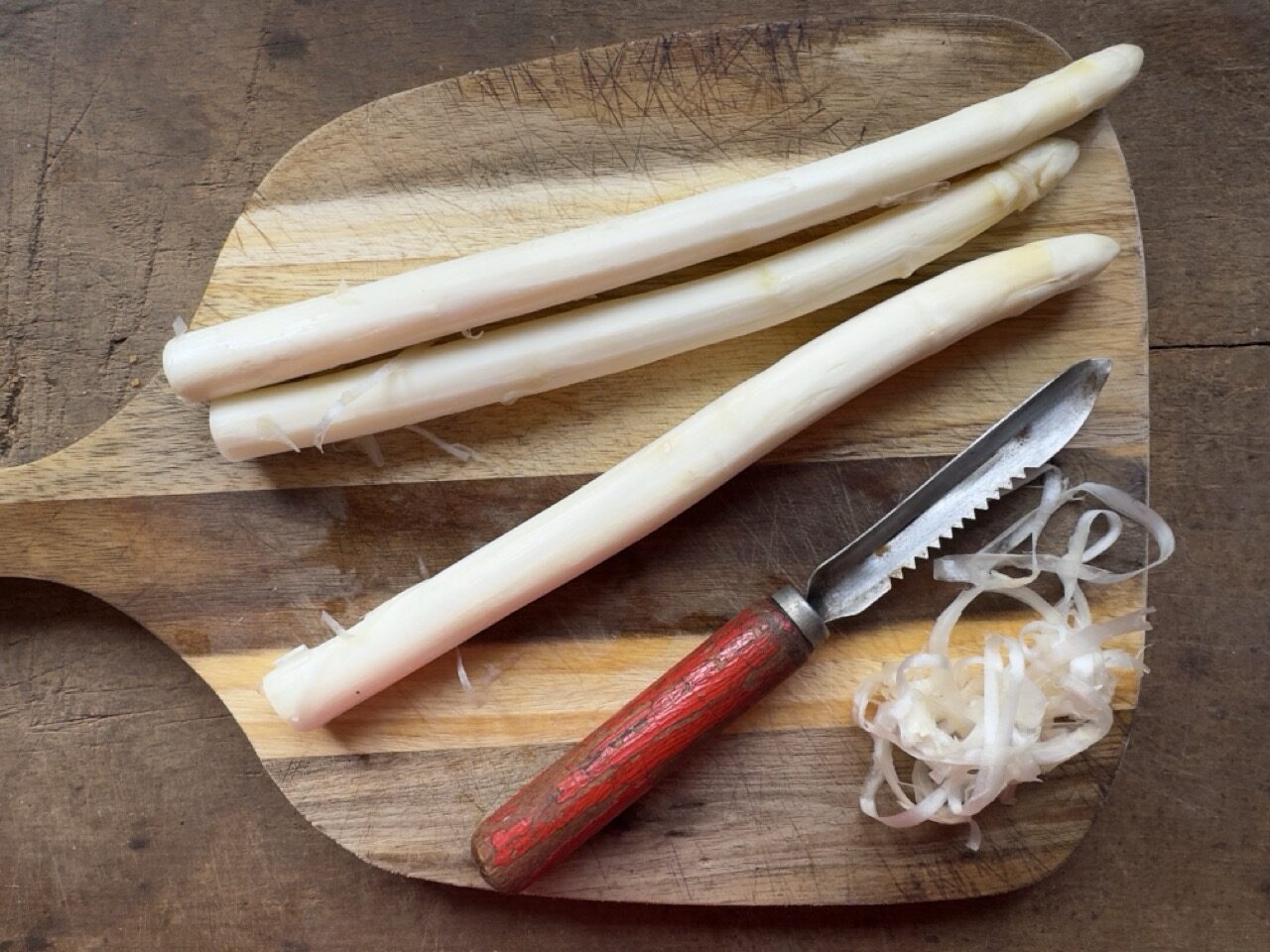 Image of peeling white asparagus on a wooden board with a rustic peeler