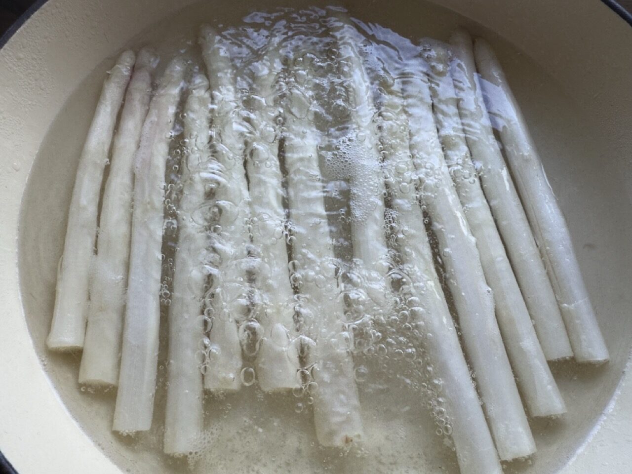 Image of white asparagus simmering in a wide cast iron pan.