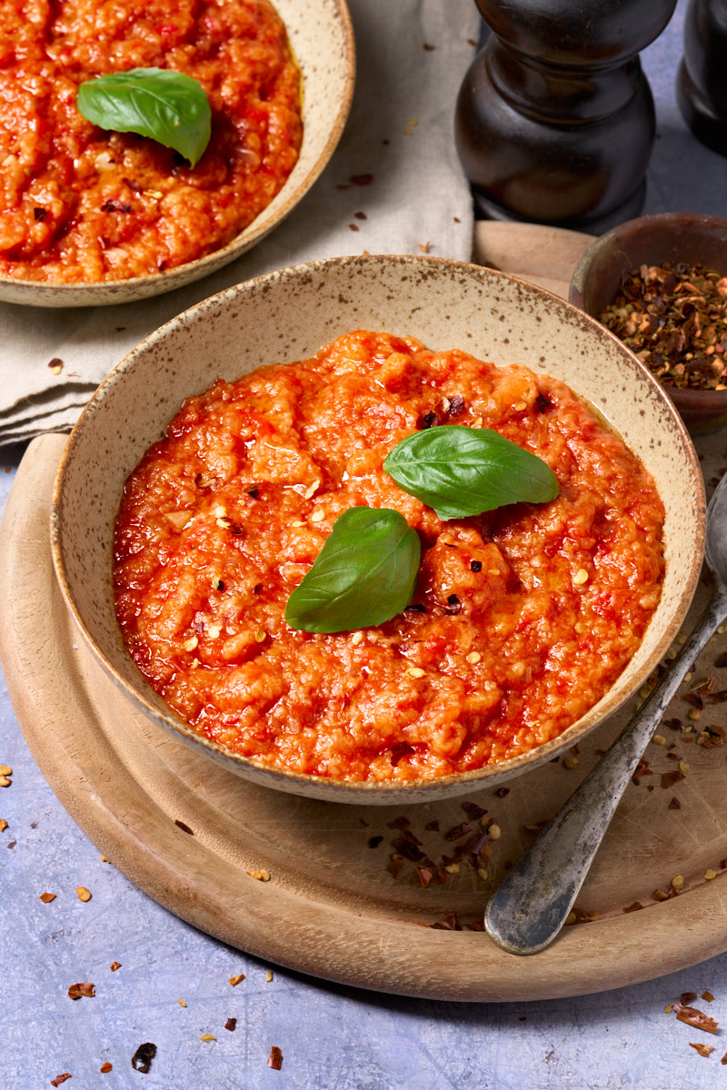image of Pappa al Pomodoro, a rustic tuscan dish made of tomatoes and stale bread, served into bowls with the red tomato soup contrasting against a light blue background.