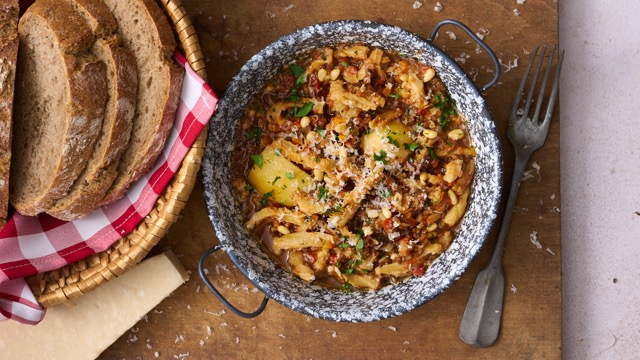 image of trippa alla genovese, a tripe dish from Liguria made with tripe, pine nuts and mushrooms in a tomato sauce served in a rustic pan on a wooden board with some crusty bread