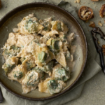 image of pansoti con salsa di noci, a Ligurian filled pasta dish of greens dressed in a walnut sauce, served in wide bowl surrounded by whole and broken walnuts and walnut pieces.