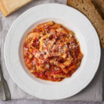 image of trippa alla firoentina, Tuscnay's signature tripe dish from Florence served on a white plate and sprinkled with parmesan cheese with bread and a block of parmesan cheese in the background