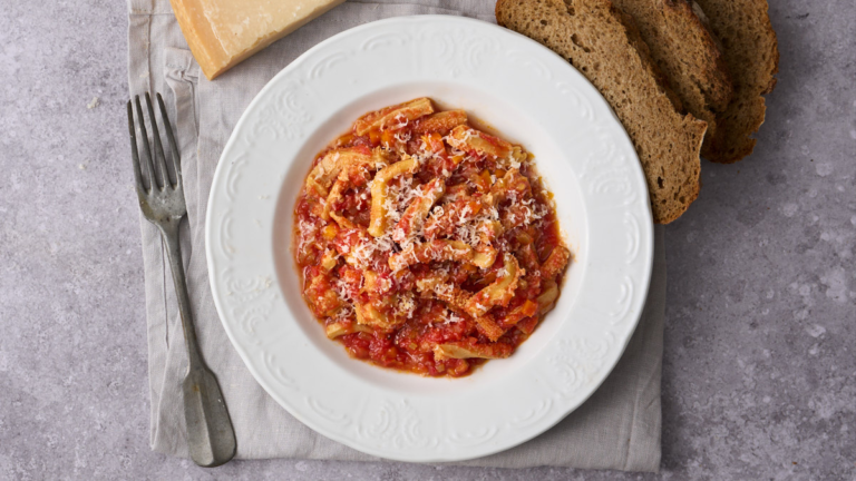 image of trippa alla firoentina, Tuscnay's signature tripe dish from Florence served on a white plate and sprinkled with parmesan cheese with bread and a block of parmesan cheese in the background