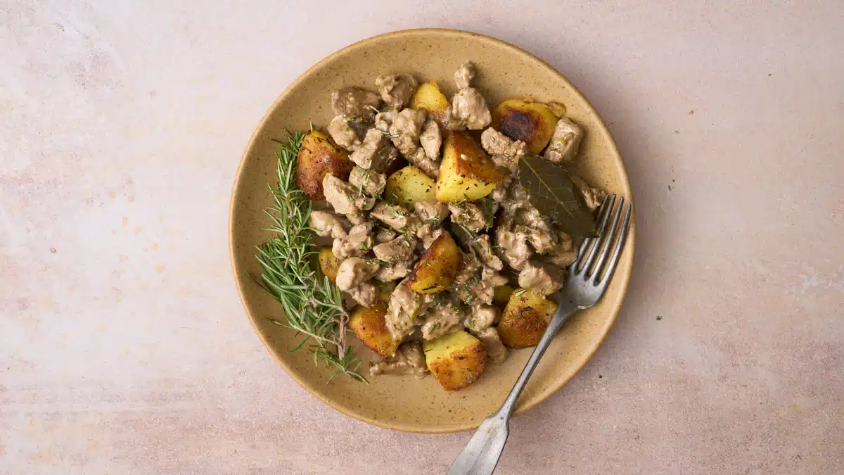Landscape image of Abbacchio alla cacciatora, a lamb stew dish with a vinegar and anchovy sauce from Rome, served on a plate of Italian rosemary roast potatoes.