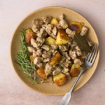 Landscape image of Abbacchio alla cacciatora, a lamb stew dish with a vinegar and anchovy sauce from Rome, served on a plate of Italian rosemary roast potatoes.