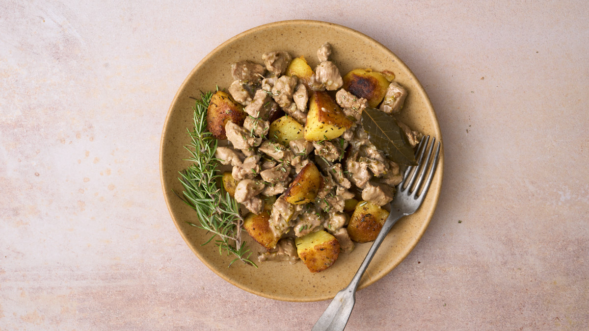 Landscape image of Abbacchio alla cacciatora, a lamb stew dish with a vinegar and anchovy sauce from Rome, served on a plate of Italian rosemary roast potatoes.