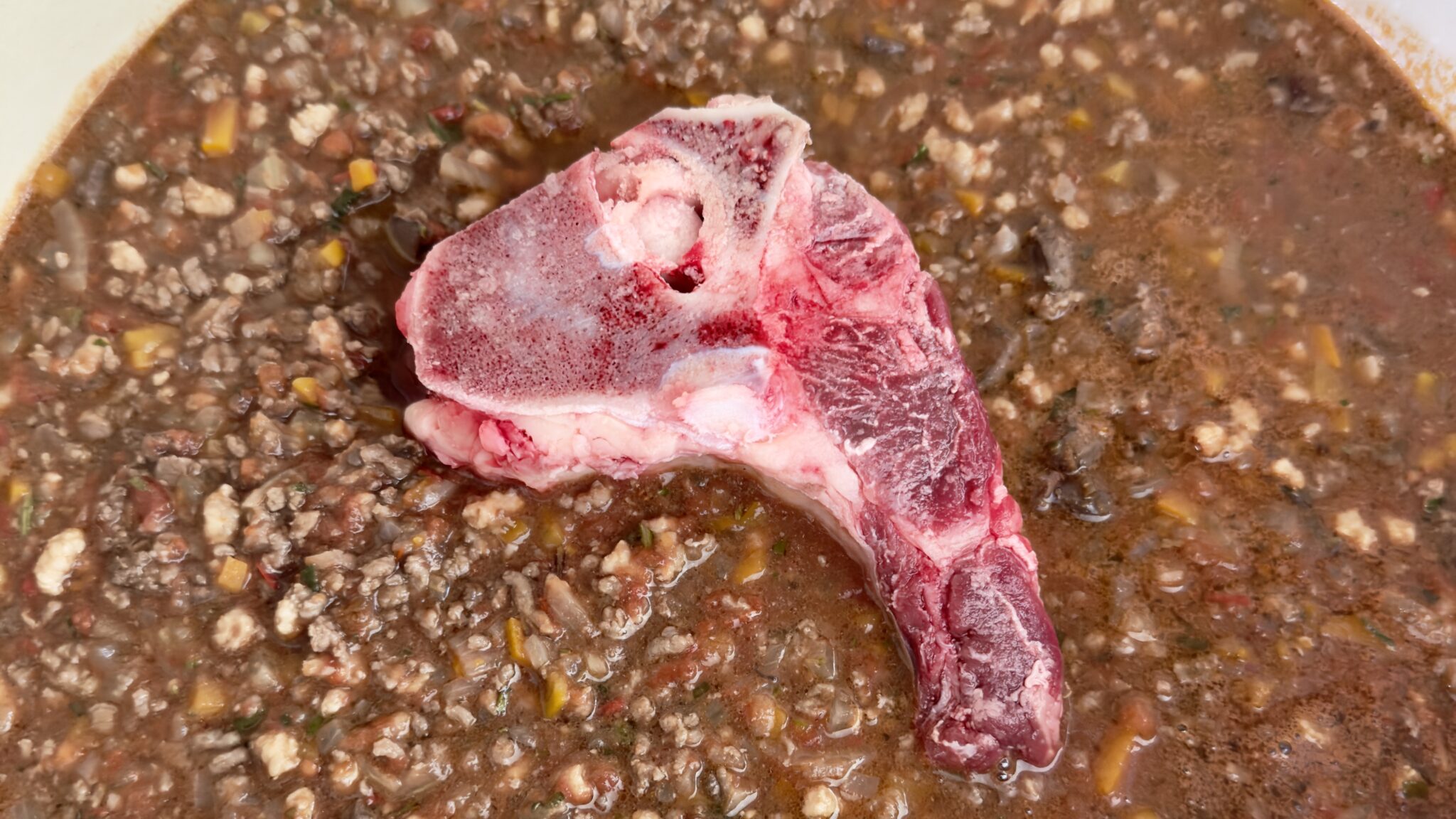image of a beef bone cooking in Ragu alla Marchigiana, a key step in building flavour in this dish