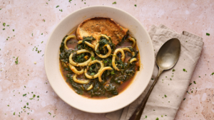 landscape image of calamari in zimino, a Ligruian stew of calamari with chard, served in a wide off white bowl with a slice of rustic toast in teh bowl soaking up all the juices.