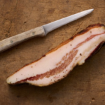 image of guanciale on a wooden board with a wooden handled knife