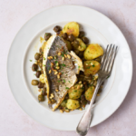 image of orate alla ligure - a ligurian sea bass dish served with potatoes, pine nuts and Taggiasca olives, served on a white plate with a clean background