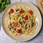 image of spaghetti mare e monti, a pasta dish with calamari rings and mushrooms, served on a wide plate next to a rustic wooden board with a wooden handled knife and some raw mushrooms. from the Marche region