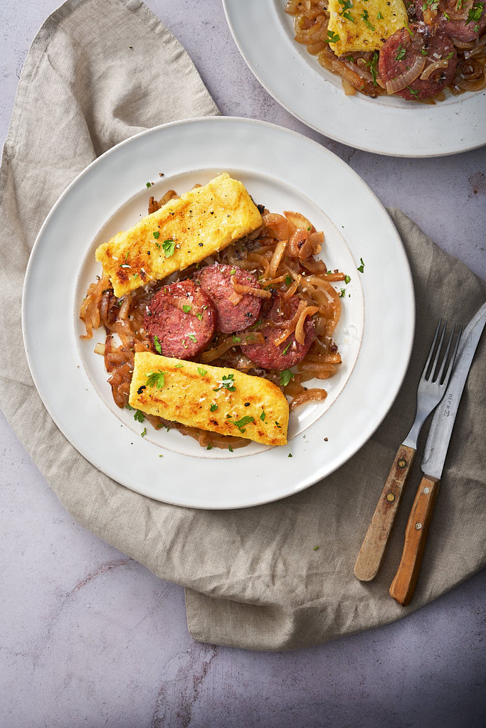 image of salame in aceto a typical Friuli dish served with polenta and sweet and sour onions, served on a white plate