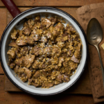 image of coratella alla marchigiana, an Easter dish from Italy's marche region made from lamb pluck (heart, lungs, liver and kidneys) served in a rustic pan on a wooden board with pecorino cheese all on a wooded table