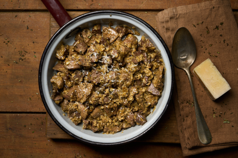 image of coratella alla marchigiana, an Easter dish from Italy's marche region made from lamb pluck (heart, lungs, liver and kidneys) served in a rustic pan on a wooden board with pecorino cheese all on a wooded table