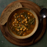 image of zemin, a traditional autumn soup of chickpeas, chard and porcini in a rustic bowl on a wooden board, served with a slice of country bread