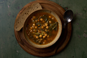 image of zemin, a traditional autumn soup of chickpeas, chard and porcini in a rustic bowl on a wooden board, served with a slice of country bread